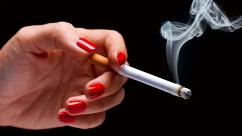 A woman's hand with painted red nails holding a smoking cigarette against a black background