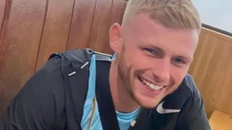 Cody Fisher, smiling, wearing a nike tracksuit and a light blue t shirt