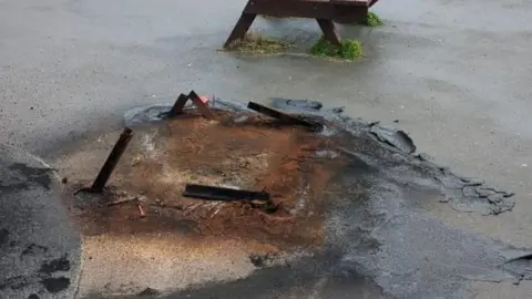 Brighton & Hove City Council A wooden bench next to damaged play equipment at a park. 