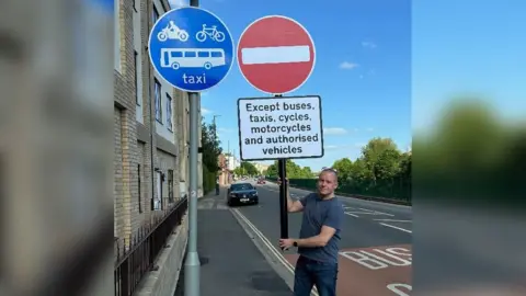 A man holds a home made "no entry" sign next to a blu