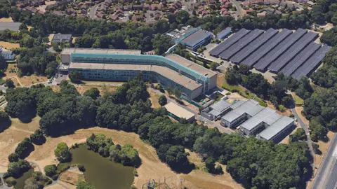 Allford Hall Monaghan Morris A bird's eye view of the Chaseside campus in Bournemouth - office buildings and behind them solar panels. In front of the offices, there is a wooded area.