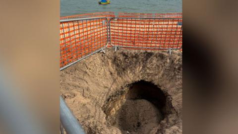 Large hole on the beach with orange cordon around it