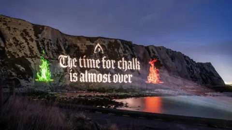 The image shows a projection on the White Cliffs of Dover with the phrase "THE TIME FOR CHALK IS ALMOST OVER" ahead of The Traitors final airing this Friday on BBC One and iPlayer.