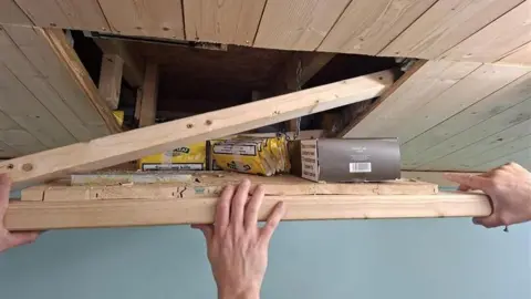 Suffolk Police A wooden hatch in a ceiling is being pulled open by three hands, inside is a quantity of packaged tobacco products - mostly Golden Virginia in yellow packets.