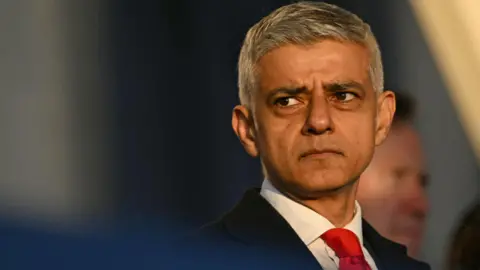 Getty Images The Mayor of London, Sir Sadiq Khan, shown from the shoulders up, looking away from the camera with a slight frown on his face. He is wearing a suit, white shirt and red tie.