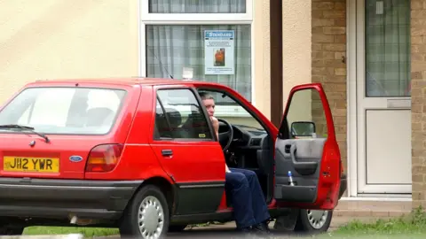 PA Media Image shows Ian Huntley biting his nails in the open driving seat of his red Ford car in 2002 while the search for the two girls was ongoing 