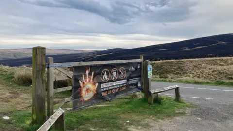 A fire service warning poster on a five-bar wooden gate and black charred moorland in the distance 