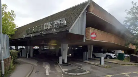 Google Google Maps shot of the High Street Car Park entrance. There's cars in the car park with barriers as you enter.