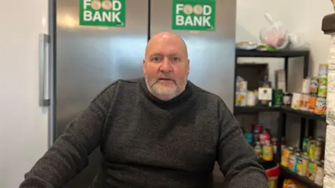 Simon Fairclough pictured wearing a grey knitted jumper looking at the camera. He is bald with a grey, short beard.