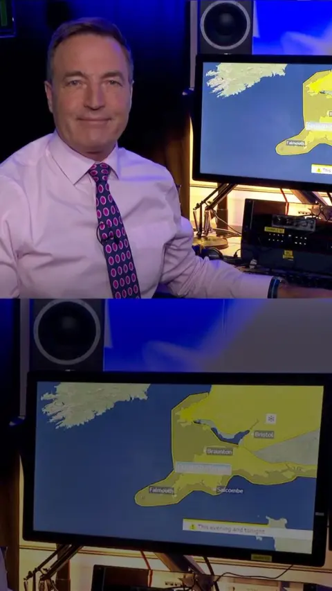 David Braine looks at the camera he is wearing a pink shirt and tie and is sat next to a weather monitor.