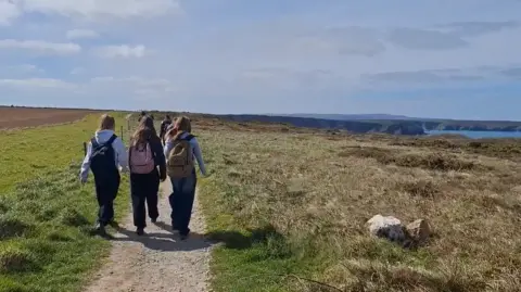 A group of teenagers walking along a coastal path. 
