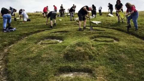 John Millar / National Trust Group of people with spades around the face of the Cerne Abbas Giant replacing its chalk.