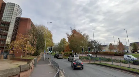 Cars driving on a ring road that has trees and buildings on either side. 