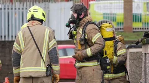 A fire fighter wearing breathing apparatus is helped by two colleagues