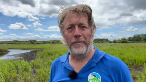 Shaun Whitmore/BBC Dave Rogers with windswept hair against the green background of Lakenheath Fen, Suffolk