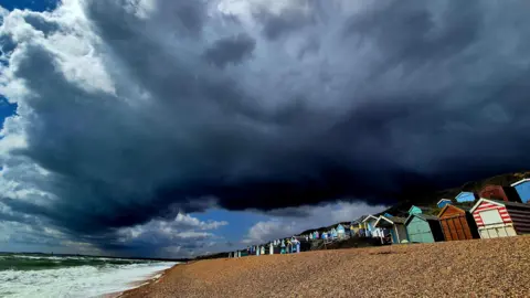 Milford on Sea, Hampshire - beach with huts in a row and low dark clouds rolling in.
