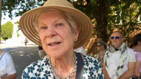 Jenny Streat wearing a summer hat and a flowery dress looking at the camera
