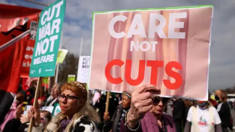 A crowd of protestors holding placards protesting against welfare cuts.