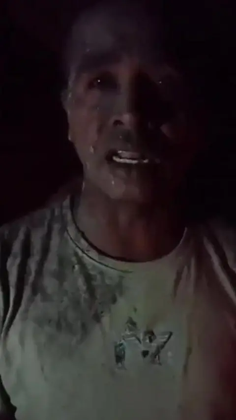 HANDOUT Ash covers a distressed-looking man's T-shirt, while bits of volcano ash are spattered on his face in a screenshot from a video