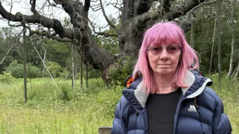 Woman with pink hair in front of tree