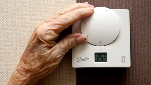 PA Media The hand of an elderly woman turning the dial of a white thermostat.