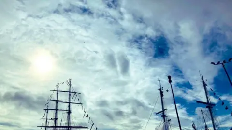 Tall ships masts against a sunny, cloudy blue sky at Aberdeen harbour.