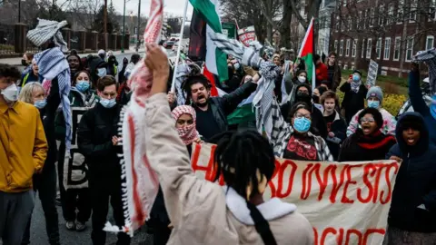 Getty Images A Harvard student addresses the crowd during a demonstration against former Israeli Prime Minister Naftali Bennett's campus visit. Studnets can be seen marching carrying pro-Palestinian flags and banners.