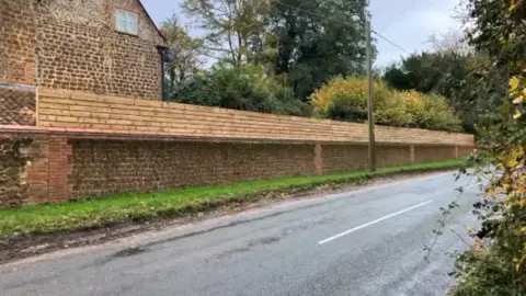 Fencing across the top of a red brick wall running alongside a road 