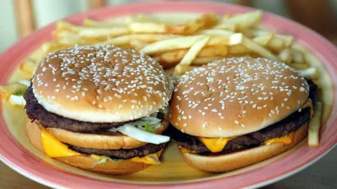 Two cheese burgers alongside chips on a plate.