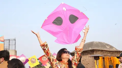 A woman holds a pink kite above her head during the Basant kite festival in Lahore, Pakistan.