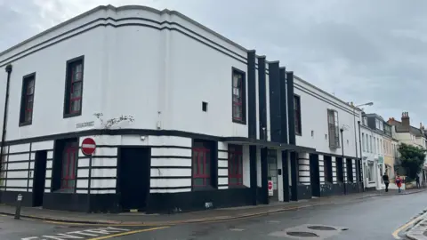 A photo of the Art Deco-style Tipsy Toad pub on New Street. The building is mainly white with black trim. The photo is taken on a grey and cloudy day. 