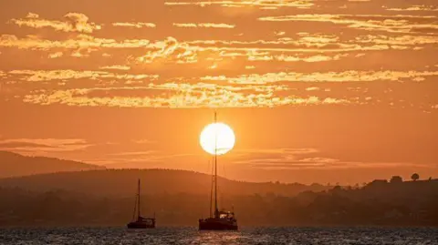 Gerard McCreesh The sunsetting over the sea. Two boats are sailing. The sky is orange.