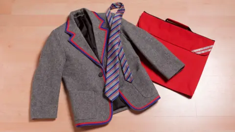 A grey school blazer with red and blue trim, a similar colour tie and a red bag