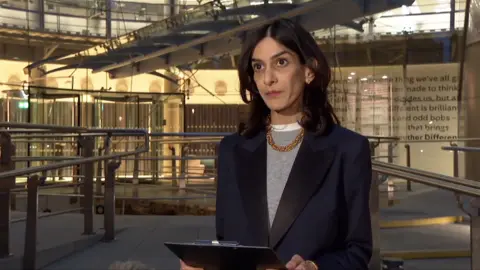 C4's Priya Dogra wearing a suit and holding a printed statement