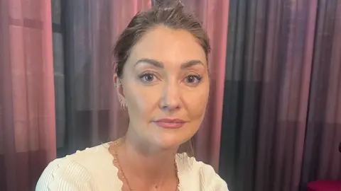 A woman with tied-back brown hair looks at the camera