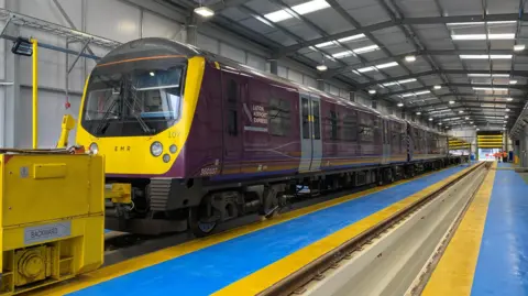 Siemens Mobility An East Midland Railway's train in a warehouse. The driver's cab is in the foreground and the carriages stretch back into the distance. next to the train there is an empty track where another train could be parked.