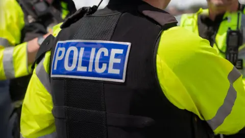 Trio of police officers on duty - stock photo.
Close-up of 'POLICE' marking written on the back of a hi-visibility stab proof vest worn by a trio of police officers at the scene of an incident.