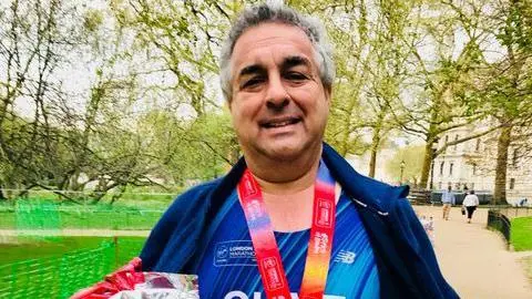 Rachel Hyman A middle-aged man with grey hair wearing running gear holding up a marathon medal
