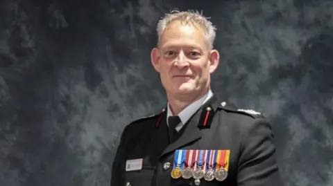 ESFRS A head and shoulders picture of Mark Matthews, who is wearing an officer's uniform with medals. The background is a photography studio.