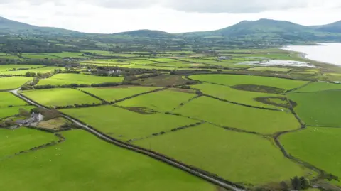 Carter Jonas Multiple fields and a few properties by the coastline can be seen in this aerial image. A mountain range can be seen in the distance.