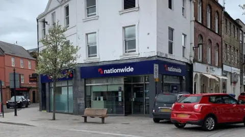 A Nationwide branch with cars parked around it and a bench in front