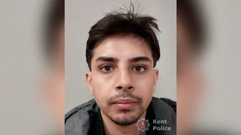 A mugshot of a man with brown hair and dark stubble. 