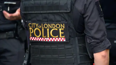 A City of London Police officer uniform in gold writing with red and white checks