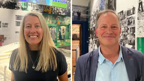 Josh McLaughlin / BBC Jody East smiles for a photograph in front of the model stadium in the gallery. Paul Mullen smiles for a photo in front of a wall documenting the club's 1983 FA Cup final game against Manchester United.