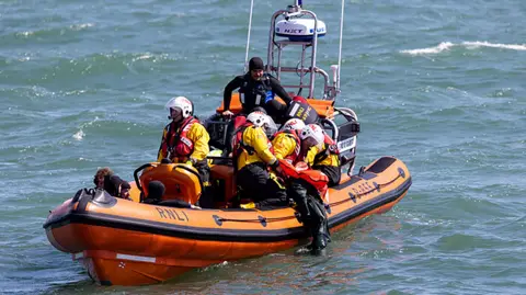 An orange RNLI lifeboat taking part in a mass rescue training exercise in Poole Bay. There are several lifeboat crew on board the RIB (rigid inflatable dinghy).