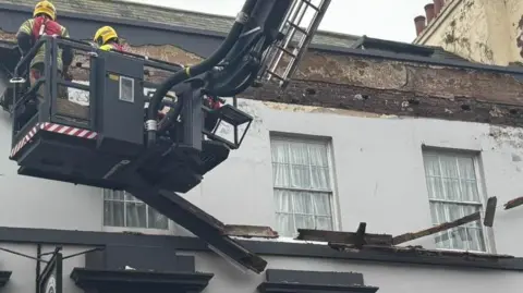 DWFRS Fire fighters in an aerial platform at the top of a building which has wood broken off its frontage