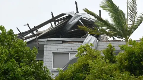 EPA The twisted, damaged roof of a holiday apartment alongside windblown trees on an unusually grey day in Australia.