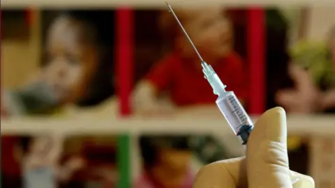 PA Media A person wearing yellow medical gloves holding a vaccination needle.