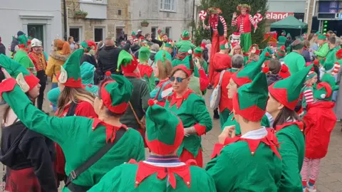 We Are Weymouth A group of people dressed in red and green elf suits in a town centre. 