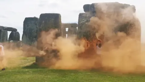 Just Stop Oil Stonehenge with a cloud of orange paint obscuring it